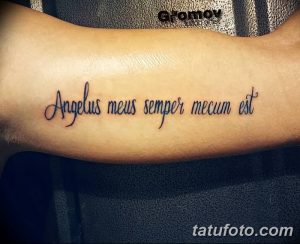 Фото тату надписи 'Angelus meus semper mecum est' на предплечье. Черная работа, каллиграфический шрифт, минималистичный дизайн.