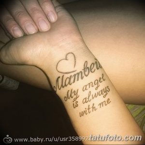 Фото тату надписи 'My angel is always with me' на запястье, с изображением сердца. Черно-серые тона, нежный дизайн, минимализм.