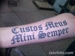 Фото татуировки на предплечье с латинской фразой 'Custos Meus Mini Semper'. Готический шрифт, черные чернила.