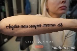 Фото татуировки на предплечье с латинской фразой 'Angelus meus semper mecum est'. Черный шрифт на светлой коже.