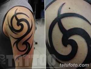 Фото тату на плече: черный трайбл узор, состоящий из плавных линий и спиралей. Минималистичный дизайн и четкая проработка.