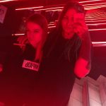 Фотография двух девушек в темном помещении с красным освещением, одна из которых демонстрирует татуировку на руке.