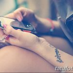 Фото минималистичной татуировки на запястье с надписью на иностранном языке. Тату выполнено тонкими линиями черного цвета.