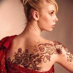 Фото тату: элегантная татуировка в стиле мехенди на спине девушки. Рисунок выполнен в черном цвете с использованием сложных узоров и орнаментов.