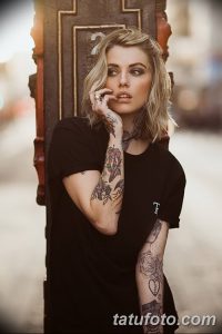 Фотография девушки в черной футболке с татуировками на руках и груди. Татуировки выполнены в стиле олд скул и изображают сердца, цветы и другие элементы.