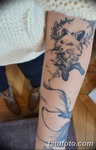 Фото татуировки с изображением лисы и летящей птицы, выполненной в черно-серых тонах на предплечье. Детализированный рисунок татуировки.