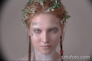 Фото девушки с татуировками на лице и шее, украшенной венком из цветов. Нежный и романтичный образ.