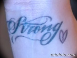 Фотография каллиграфической татуировки надписи 'Strong' с изображением сердца на руке. Изображение демонстрирует татуировку крупным планом, показывая детали и стиль исполнения.