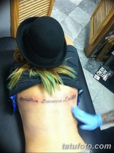 Фотография татуировки с именем 'Demetria Devonne Lovato' на спине женщины. Изображение сделано крупным планом, акцент на шрифте и расположении татуировки.