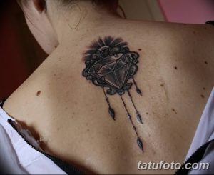 Фото тату бриллианта в декоративной рамке на спине. Черно-белый рисунок татуировки с элементами готики.