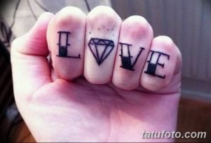 Фото тату надписи LOVE с бриллиантом вместо буквы O на пальцах. Минималистичный рисунок татуировки, выполненный черными чернилами.