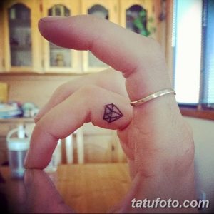 Фото микро тату с изображением небольшого черного бриллианта на пальце руки. Идеальный выбор для тех, кто ценит минимализм и лаконичность.