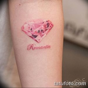 Фото тату: нежный розовый бриллиант в акварельной технике с надписью "Romantic" на предплечье. Элегантный и женственный рисунок татуировки.