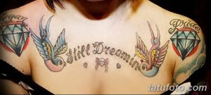 Фото тату на груди с двумя ласточками, бриллиантами и надписью 'Still Dreaming'. Яркие цвета и традиционный стиль.