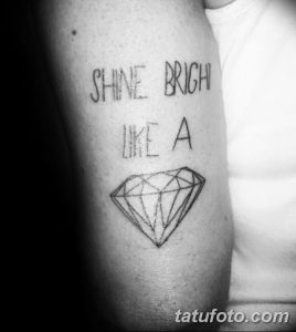 Фото тату: надпись "SHINE BRIGHT LIKE A" над изображением бриллианта на плече, выполненное в черном цвете.