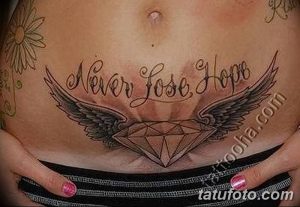 Фото татуировки на животе: бриллиант с крыльями, окруженный надписью 'Never Lose Hope'.