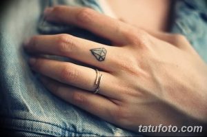 Фото тату: крошечный черный бриллиант на безымянном пальце женской руки. Минималистичный рисунок татуировки.