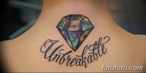Фото татуировки бриллианта на затылке с надписью 'Unbreakable'. Цветная татуировка с использованием ярких оттенков и каллиграфического шрифта.