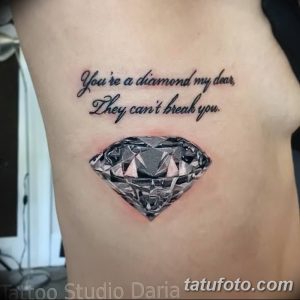 Фото тату бриллианта на боку с надписью 'You're a diamond my dear, They can't break you'. Черно-белый рисунок татуировки с четкими линиями.