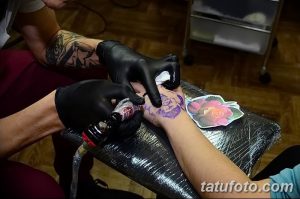 Фото процесса нанесения татуировки с изображением цветка розы на запястье. Мастер в черных перчатках работает машинкой.