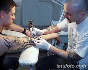 Фотография процесса нанесения татуировки в стиле традишнл с изображением волков на руке, мастер работает тату-машинкой.