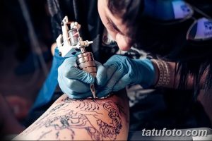 Фотография процесса нанесения сложной татуировки с изображением дракона на руке, мастер работает тату-машинкой в перчатках.