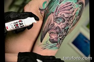 Фото процесса нанесения заживляющего средства на свежую татуировку. Мастер в черных перчатках аккуратно обрабатывает рисунок.