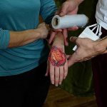 Фото свежей татуировки в виде красной розы на руке, обернутой защитной пленкой. Видны детали рисунка и процесс ухода за татуировкой.