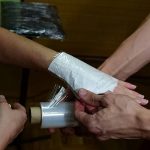 Фото процесса обертывания свежей татуировки на руке прозрачной защитной пленкой. Мастер тату аккуратно наносит пленку, обеспечивая гигиеническую защиту рисунка.