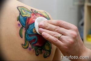 Фото процесса ухода за свежей татуировкой на плече. Мастер обрабатывает тату ватным диском.