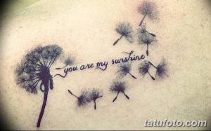 Фото тату одуванчика с надписью "you are my sunshine" на плече. Рисунок выполнен в черно-белой гамме.