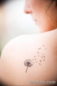 Фото минималистичной татуировки одуванчика на лопатке. Черно-белый рисунок татуировки, выполненный в тонких линиях, символизирующий легкость и свободу.
