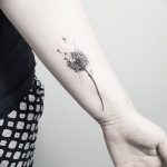Фото небольшой татуировки одуванчика на запястье. Черно-белый рисунок, выполненный тонкими линиями, выглядит очень нежно и изящно.