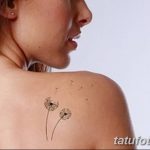 Фотография татуировки одуванчика с улетающими пушинками, расположенной на плече. Изображение выполнено в черно-серых тонах, с акцентом на детализацию.