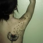 Фото тату одуванчика на спине и лопатке. Черно-белый рисунок татуировки выполнен в реалистичном стиле с акцентом на детализацию и динамику.
