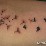 Фото тату одуванчика, из которого вылетают птицы, на предплечье. Изящный рисунок в черных тонах, символизирующий свободу и мечты.