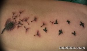 Фото тату одуванчика, из которого вылетают птицы, на предплечье. Изящный рисунок в черных тонах, символизирующий свободу и мечты.