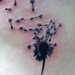 Фото тату одуванчика, из которого разлетаются семена, на коже. Минималистичный дизайн в черных тонах, символизирующий свободу.