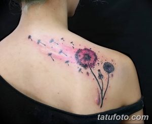 Акварельная татуировка одуванчика с летящими семенами на плече. Изображение выполнено в розовых и серых тонах, создавая мягкий и романтичный вид.