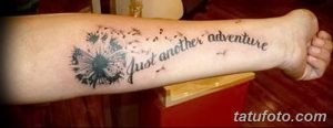Фото тату одуванчика с летящими семенами и надписью 'just another adventure' на предплечье, выполненное в черно-серых тонах.