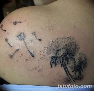 Фото тату одуванчика с пушинками на плече. Черно-белый рисунок татуировки выполнен в реалистичном стиле с проработкой деталей.