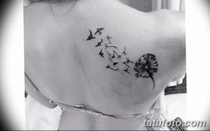 Фото татуировки на плече с изображением одуванчика, из которого вылетают птицы, выполненное тонкими черными линиями в минималистичном стиле.