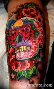 Фото тату в стиле sugar skull с ярким черепом, украшенным цветами и узорами. Татуировка выполнена на руке в яркой цветовой гамме.