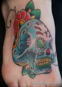 Фото тату: черно-белый рисунок черепа с цветком на лодыжке. Небольшой эскиз тату в минималистичном стиле.