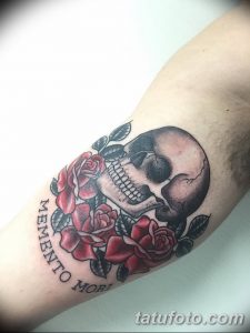 Фото тату с изображением черепа, окруженного красными розами и надписью 'Memento Mori' на руке. Детализированный рисунок татуировки в традиционном стиле.