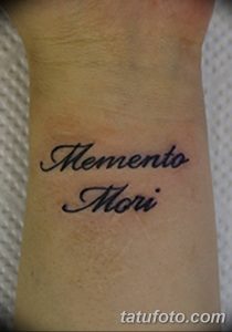 Фото тату надписи 'Memento Mori' выполненной классическим шрифтом на предплечье. Черно-белая татуировка с четкими контурами.