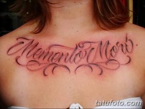 Фото тату с надписью 'Memento Mori' и декоративными завитками на груди. Черно-серая татуировка с детализированным дизайном.