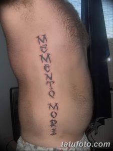 Фото тату с вертикальной надписью 'Memento Mori' на боку. Простой, лаконичный рисунок татуировки черным цветом.