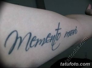 Фото тату с надписью 'Memento Mori', выполненной изящным курсивом на руке. Стильная и минималистичная татуировка, привлекающая внимание своей каллиграфией.