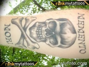 Фото тату на руке: классический череп с перекрещенными костями в стиле олдскул. Черно-белая татуировка, простая и лаконичная.